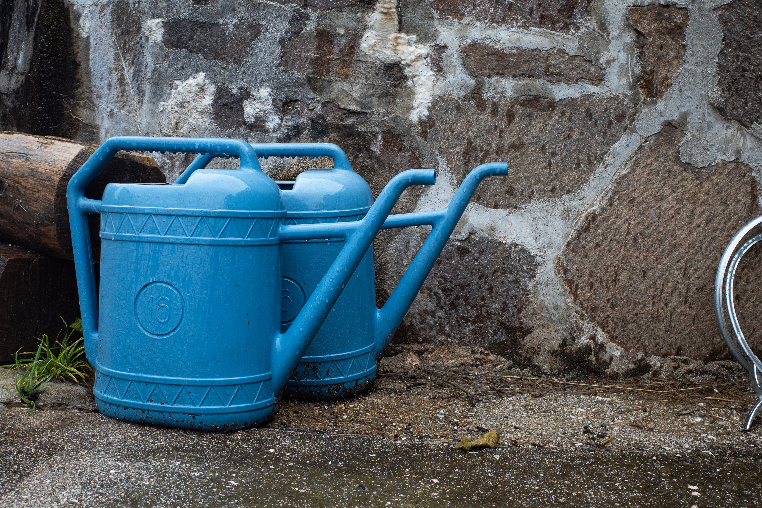 Zwei blaue Gießkannen an der Bruchsteinmauer